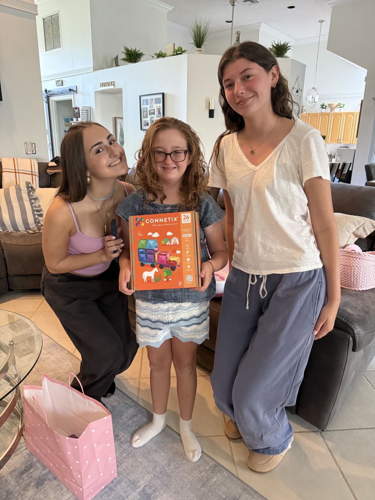 A girl holding a birthday gift between two smiling teen volunteers