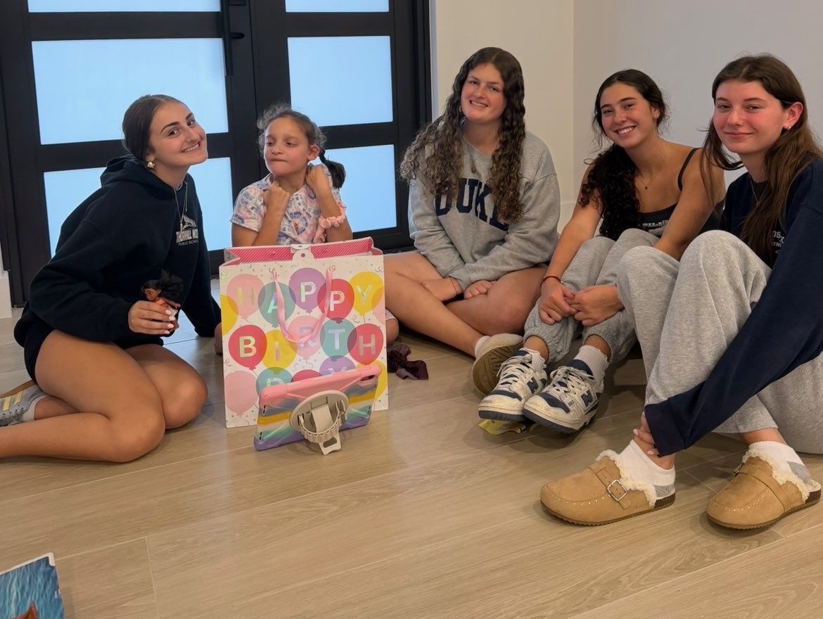 Four teen volunteers sitting on the floor with a young girl and her birthday gift bag