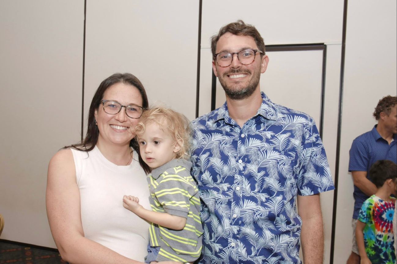 A mother and father smiling with their toddler at a Chanukah gathering