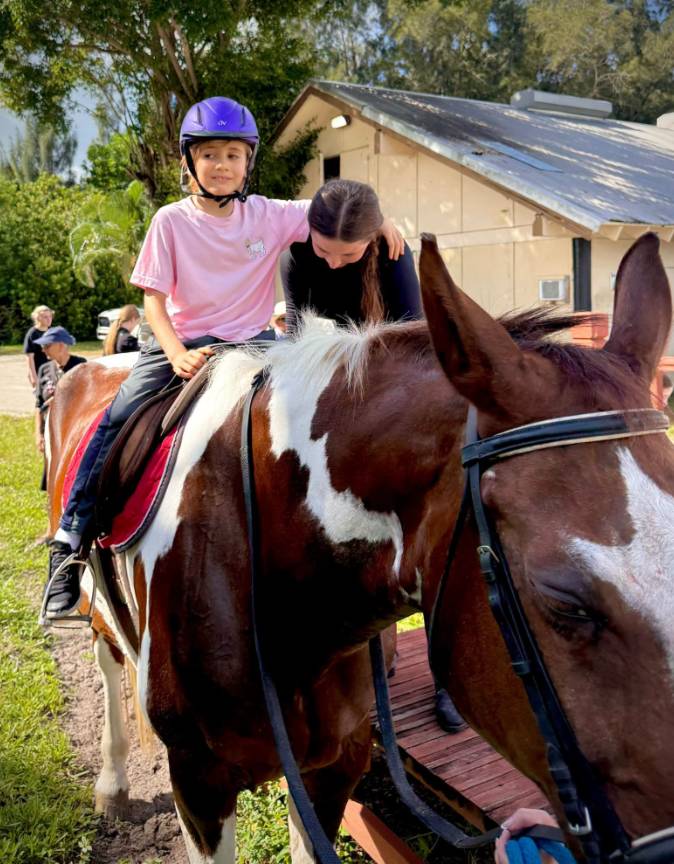 A child in a purple helmet riding a horse with a volunteer beside her