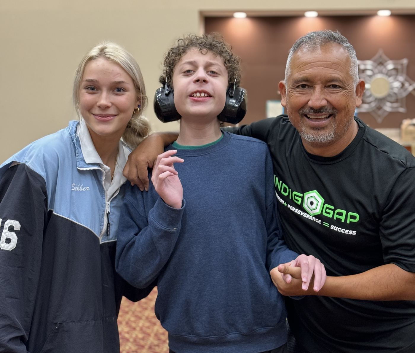 A coach and a teen volunteer smiling with a participant wearing ear defenders at Sports Circle