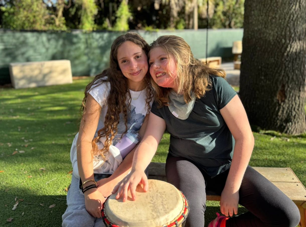 A teen volunteer and her friend playing a drum together outdoors
